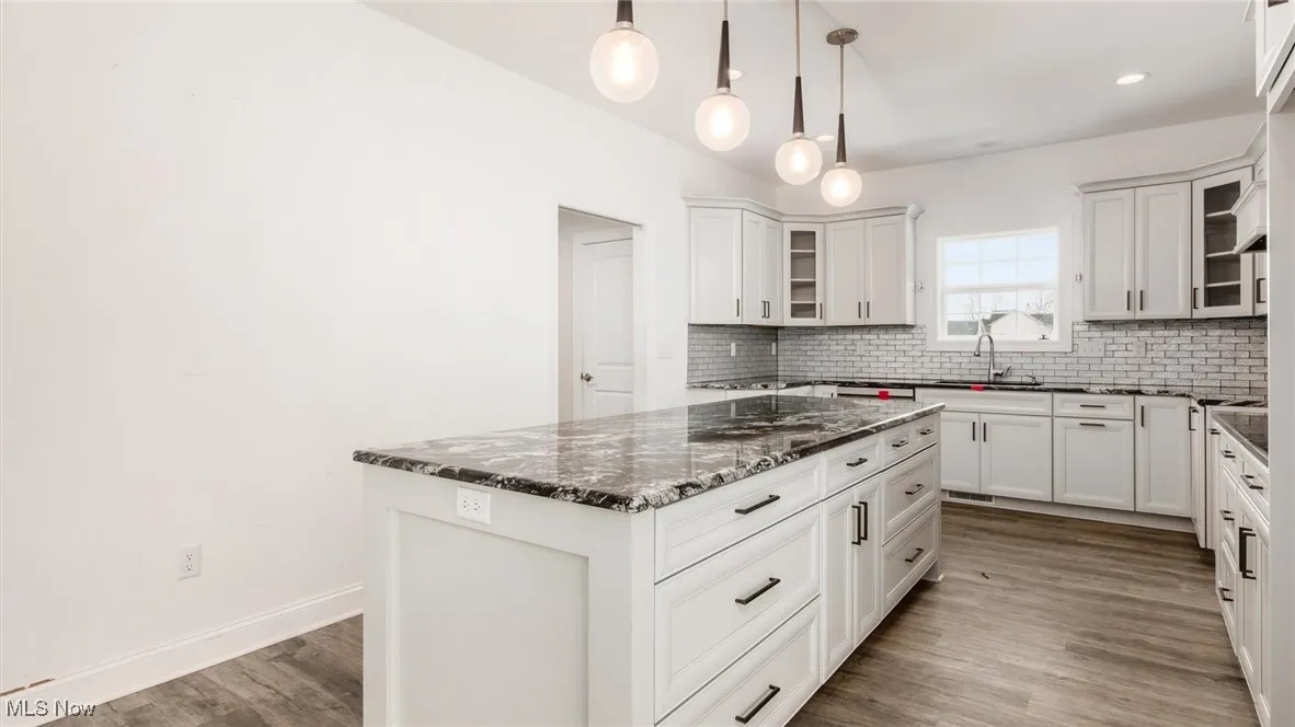 Kitchen featuring glass insert cabinets, dark stone countertops, backsplash, decorative light fixtures, and recessed lighting