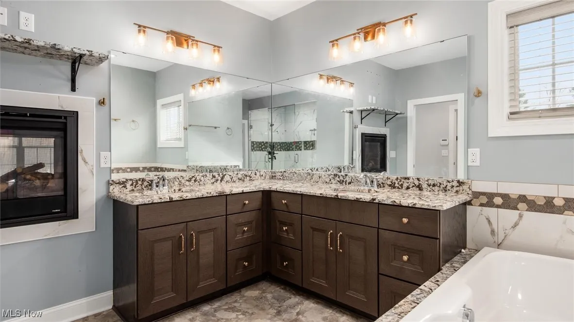 Full bath with a multi sided fireplace, double vanity, a garden tub, and a stall shower