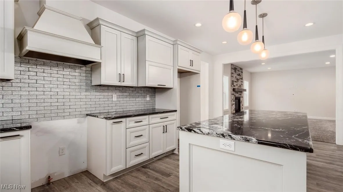 Kitchen featuring custom range hood, decorative backsplash, dark stone counters, decorative light fixtures, and a kitchen island