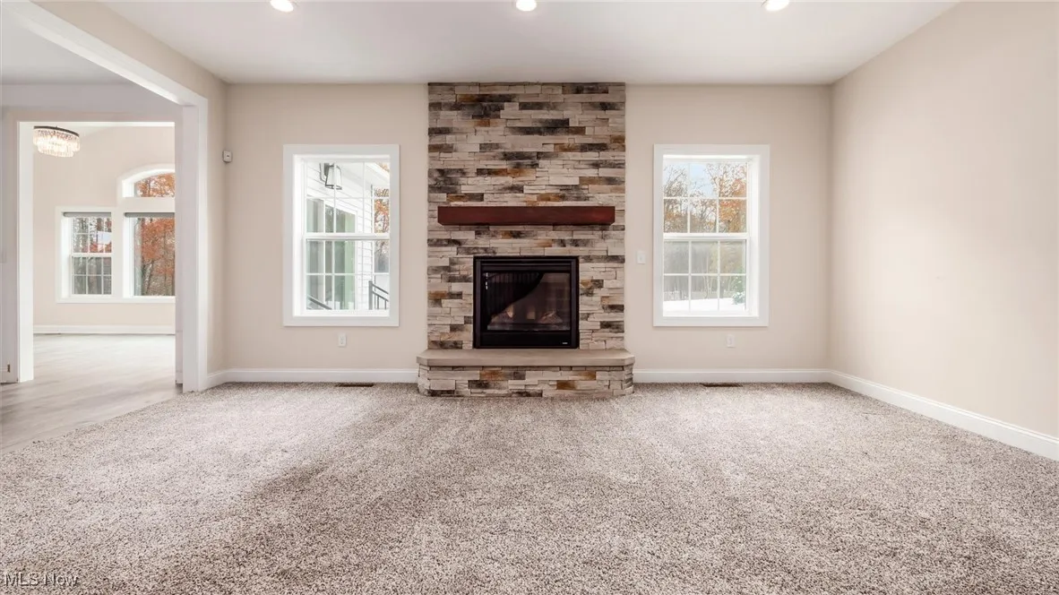 Unfurnished living room featuring carpet flooring, a stone fireplace, plenty of natural light, and recessed lighting