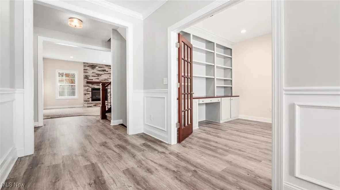 Hall with a desk, a wainscoted wall, light wood-style flooring, a decorative wall, and ornamental molding