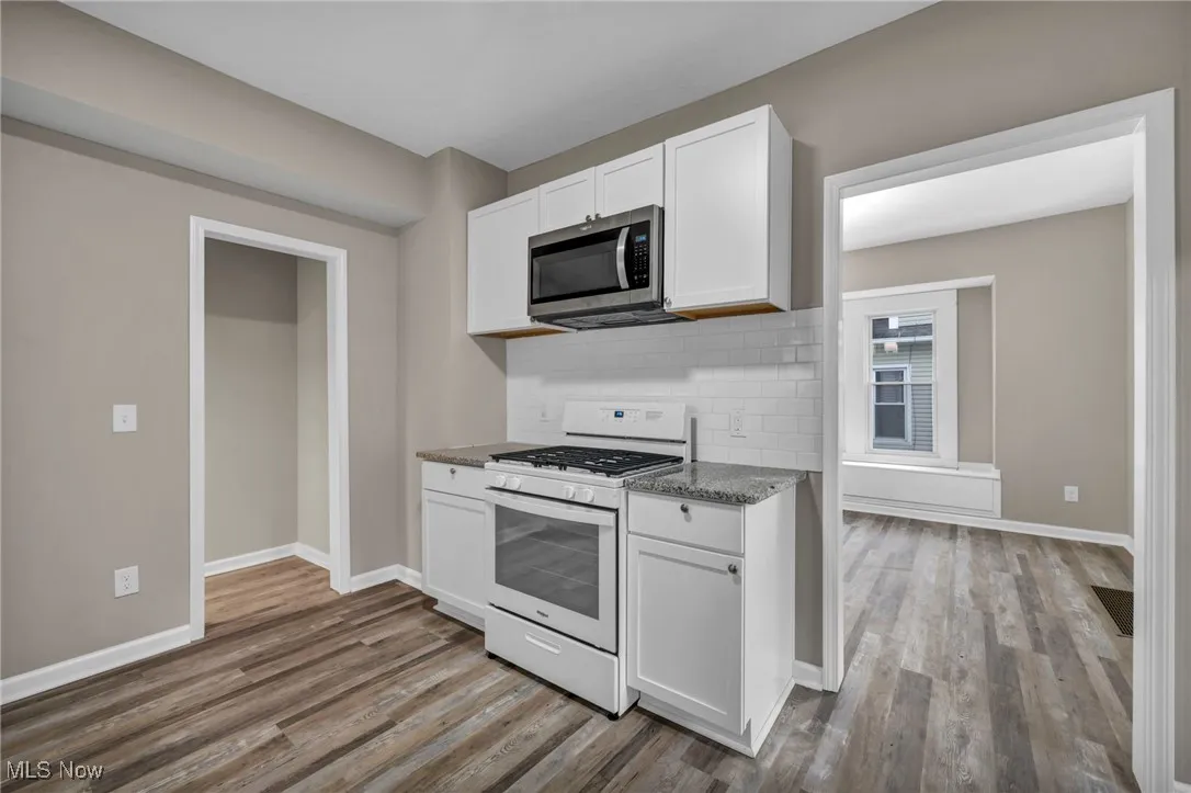 Kitchen featuring white gas stove, dark stone counters, white cabinetry, and backsplash