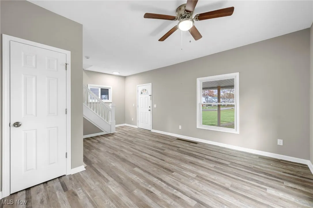 Unfurnished room featuring light wood-type flooring, a ceiling fan, and stairs