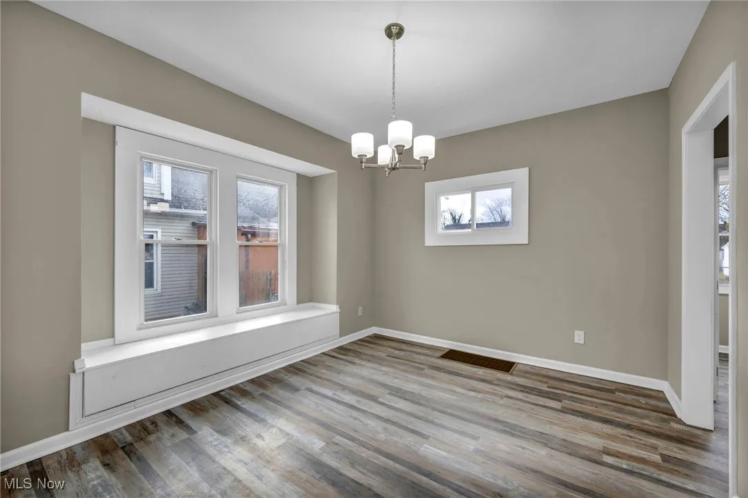 Empty room featuring healthy amount of natural light, wood finished floors, and a chandelier