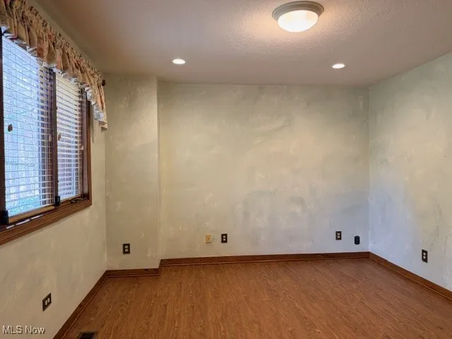 Empty room featuring dark wood-style floors, a textured ceiling, a textured wall, and recessed lighting