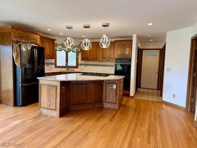 Kitchen with a center island, brown cabinets, decorative backsplash, black appliances, and pendant lighting