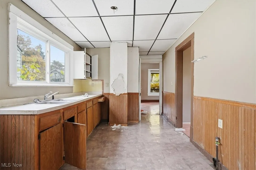 Kitchen featuring a drop ceiling, wood walls, a wainscoted wall, light countertops, and brown cabinets