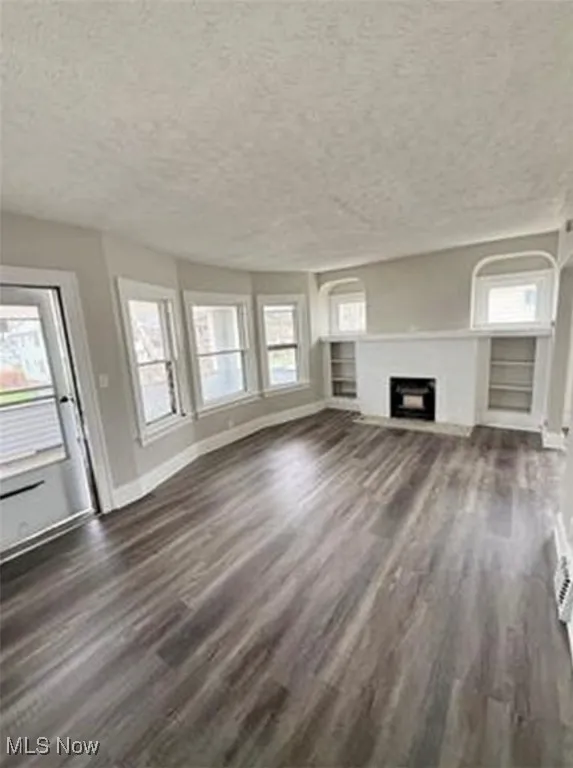 Unfurnished living room with a textured ceiling, dark wood-type flooring, and a fireplace