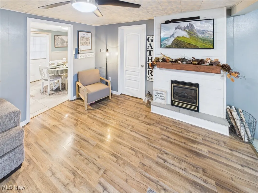 Living area with a glass covered fireplace, light wood-style floors, and ceiling fan