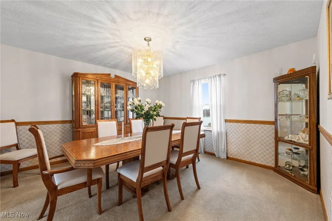 Dining space featuring wainscoting, a textured ceiling, light carpet, and a chandelier