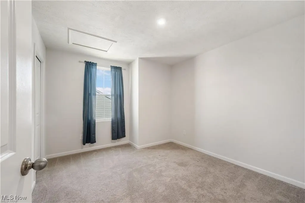 Spare room featuring attic access, light colored carpet, and a textured ceiling