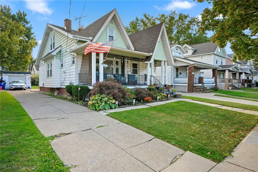 Bungalow-style home featuring a front lawn, a porch, roof with shingles, an outbuilding, and a garage