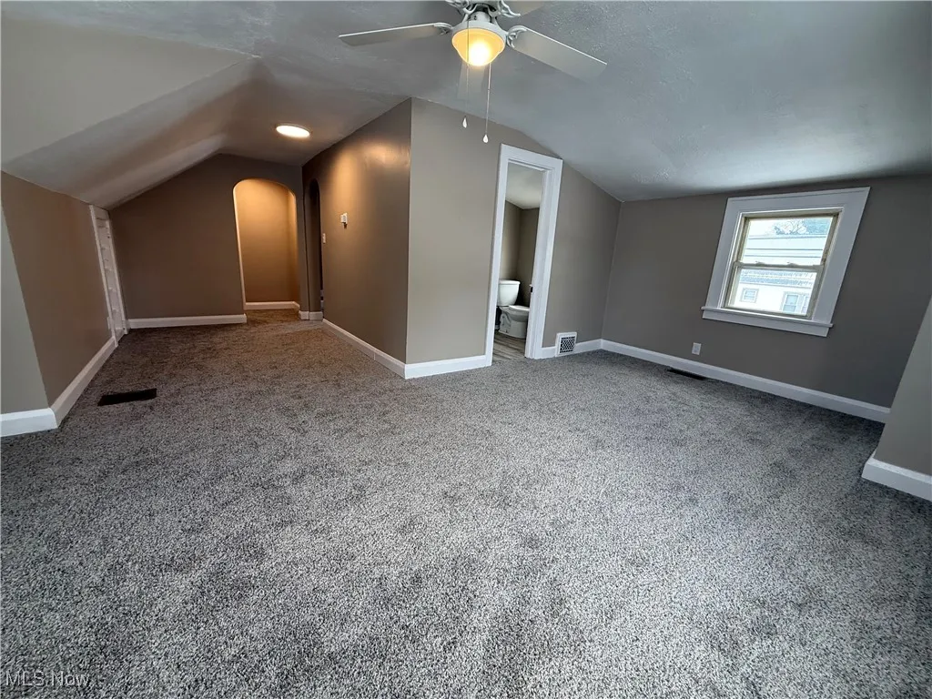 bed room with light colored carpet, lofted ceiling, and arched walkways