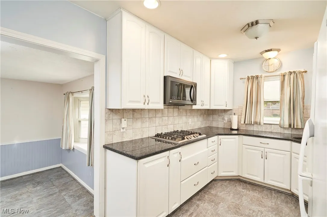 Kitchen with appliances with stainless steel finishes, white cabinets, wainscoting, decorative backsplash, and dark stone countertops