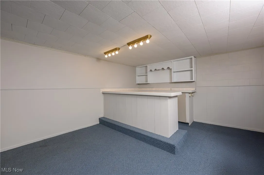 Kitchen featuring light countertops, a peninsula, dark colored carpet, open shelves, and white cabinets