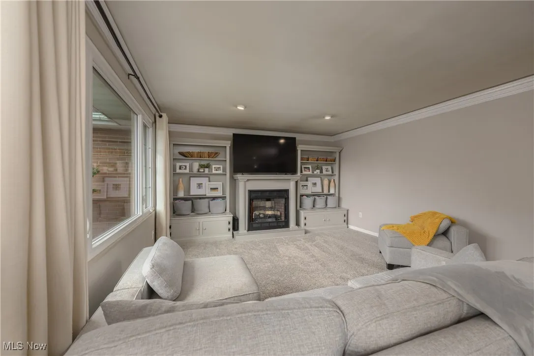 Living area with a glass covered fireplace, carpet flooring, and crown molding