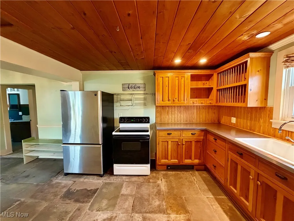 Kitchen with electric range oven, freestanding refrigerator, light countertops, open shelves, and wood ceiling