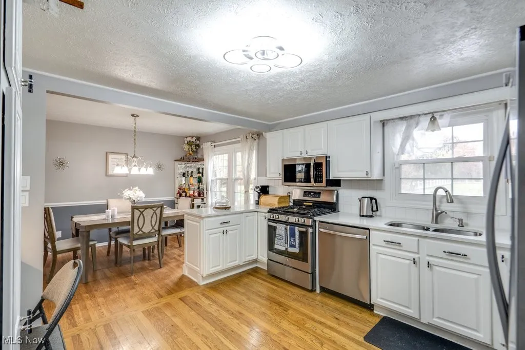 Kitchen featuring stainless steel appliances, light wood-style flooring, white cabinets, decorative light fixtures, and healthy amount of natural light