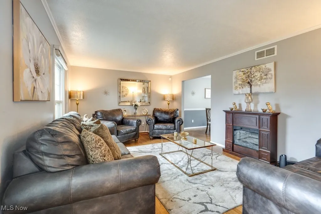 Living room with crown molding, wood finished floors, and a glass covered fireplace