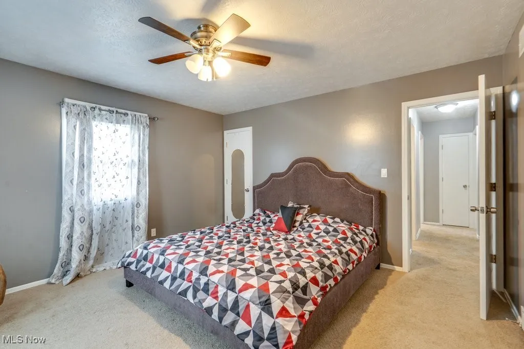 Bedroom with a textured ceiling, light colored carpet, and a ceiling fan