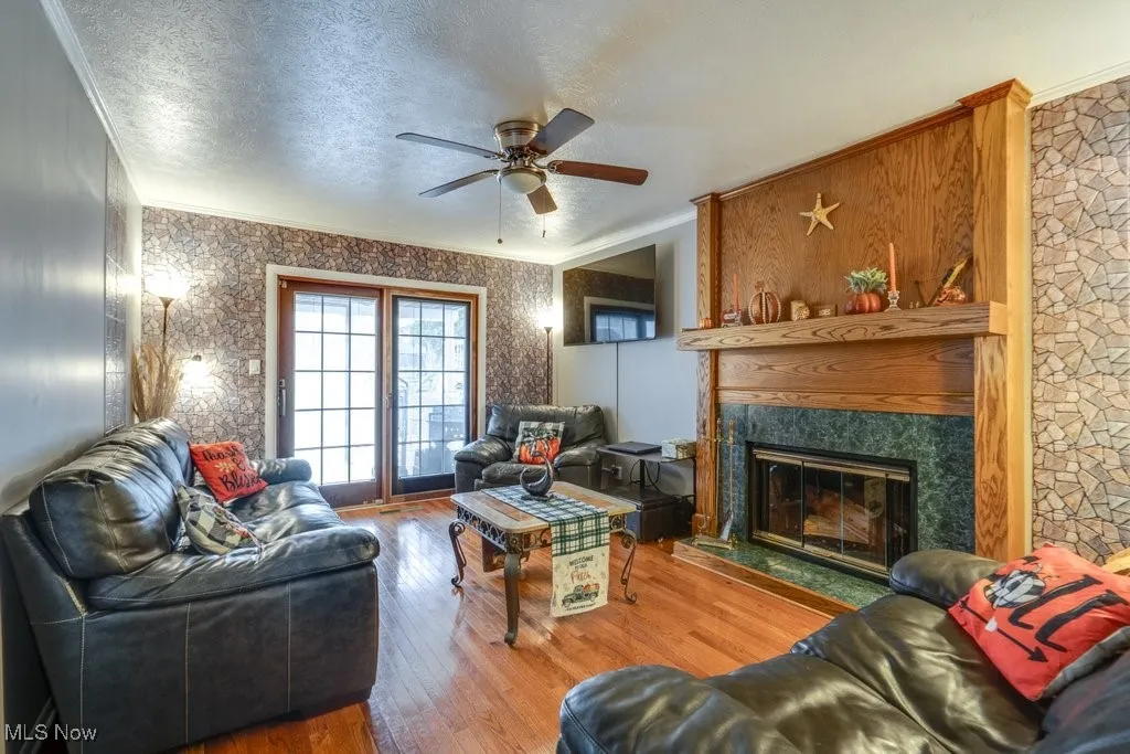Living area with crown molding, hardwood / wood-style floors, a textured ceiling, wallpapered walls, and a fireplace