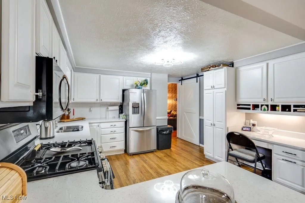 Kitchen featuring a barn door, white cabinetry, appliances with stainless steel finishes, decorative backsplash, and a textured ceiling