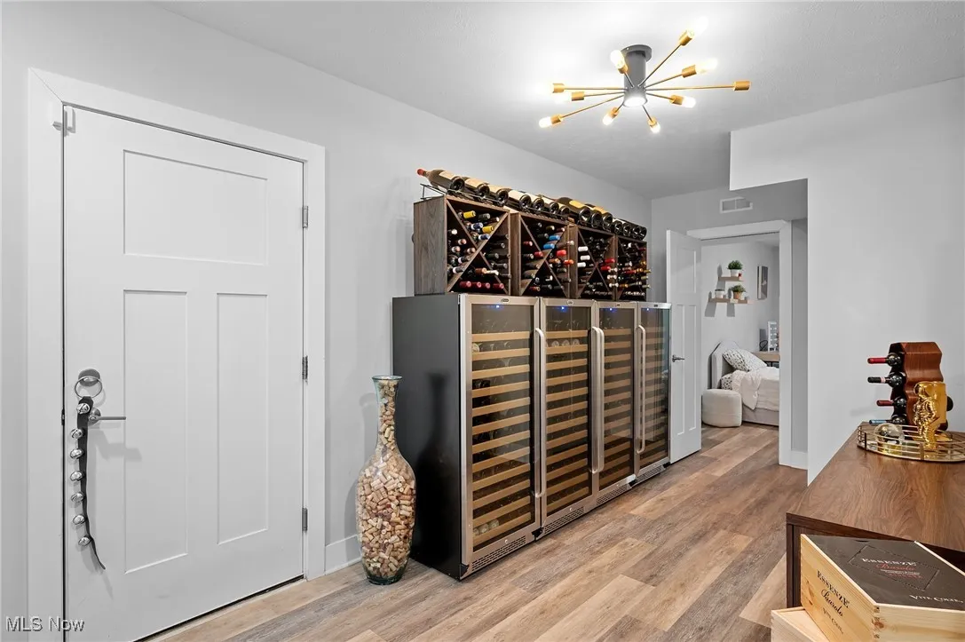 Wine area with beverage cooler, a chandelier, and light wood finished floors