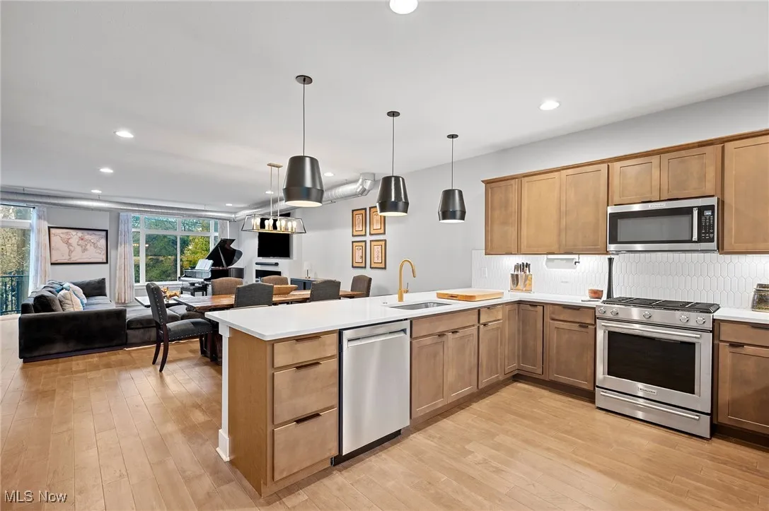 Kitchen with stainless steel appliances, open floor plan, recessed lighting, hanging light fixtures, and light wood-style flooring