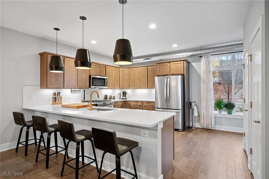 Kitchen with light countertops, a peninsula, tasteful backsplash, appliances with stainless steel finishes, and a breakfast bar