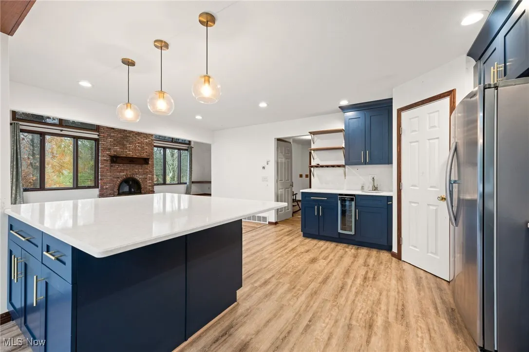 Kitchen with blue cabinetry, freestanding refrigerator, hanging light fixtures, open shelves, and light wood finished floors