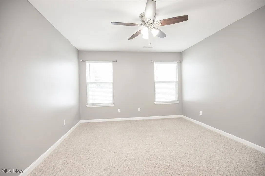 Unfurnished room featuring light carpet, plenty of natural light, and a ceiling fan