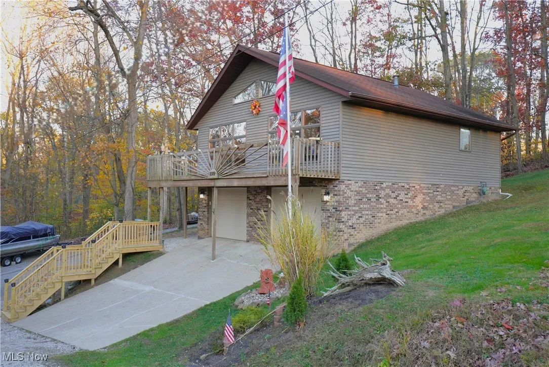 View of side of property featuring concrete driveway, a garage, a deck, brick siding, and stairway