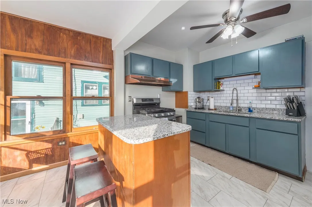 Kitchen with granite counters, decorative backsplash, a kitchen island, blue cabinetry, and stainless steel range with gas stovetop