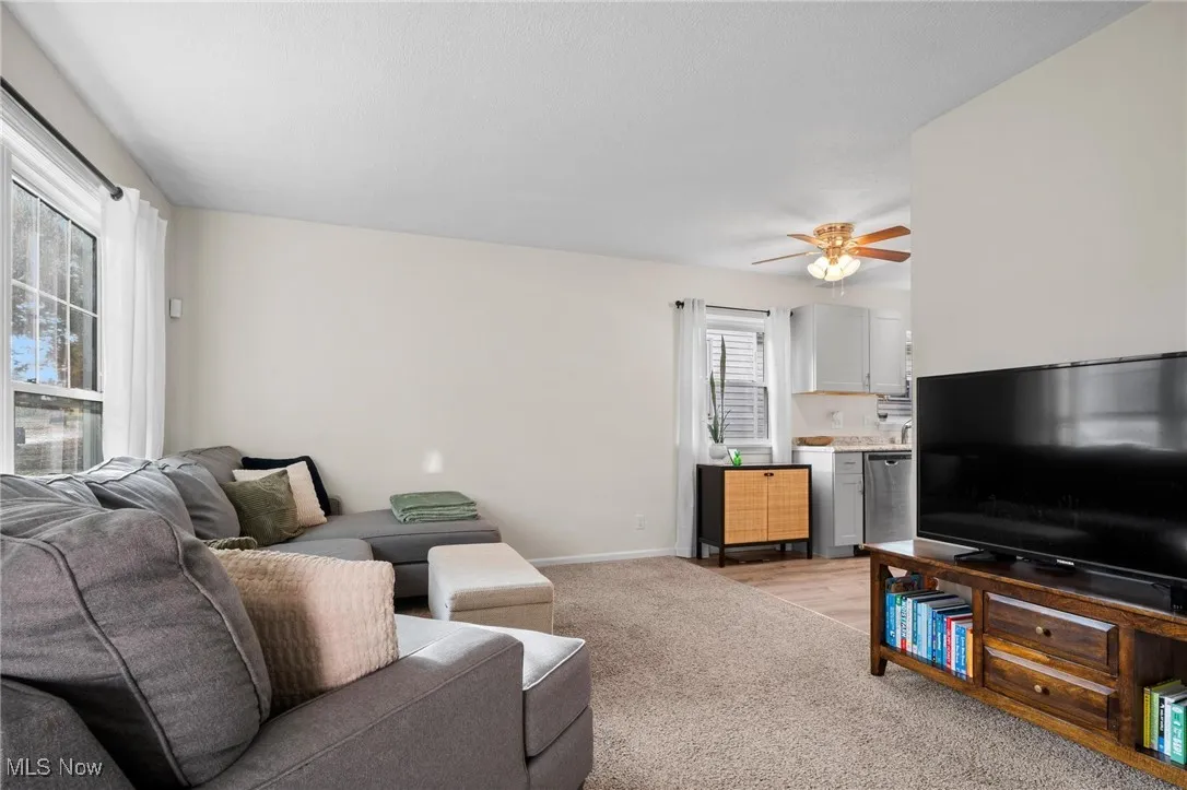 Living area with ceiling fan, light carpet, and light wood finished floors
