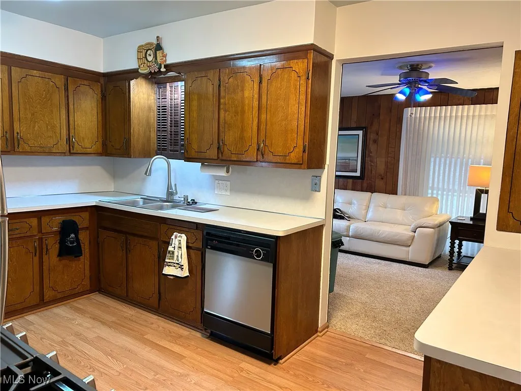 Kitchen featuring light countertops, stainless steel dishwasher, open floor plan, ceiling fan, and brown cabinets
