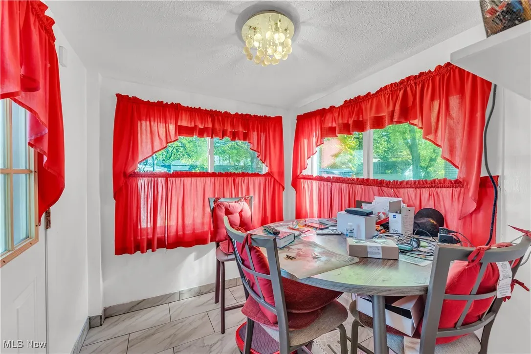 Dining area with plenty of natural light, light marble finish floors, a chandelier, and a textured ceiling