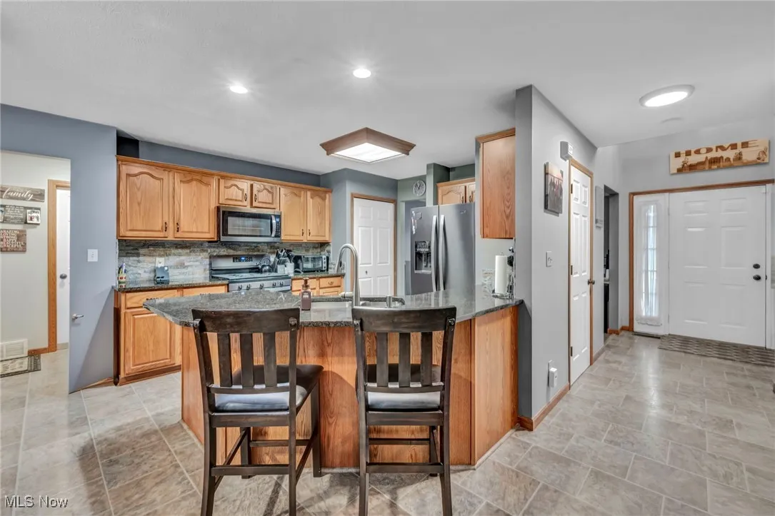 Kitchen with a peninsula, dark stone countertops, appliances with stainless steel finishes, backsplash, and a kitchen breakfast bar