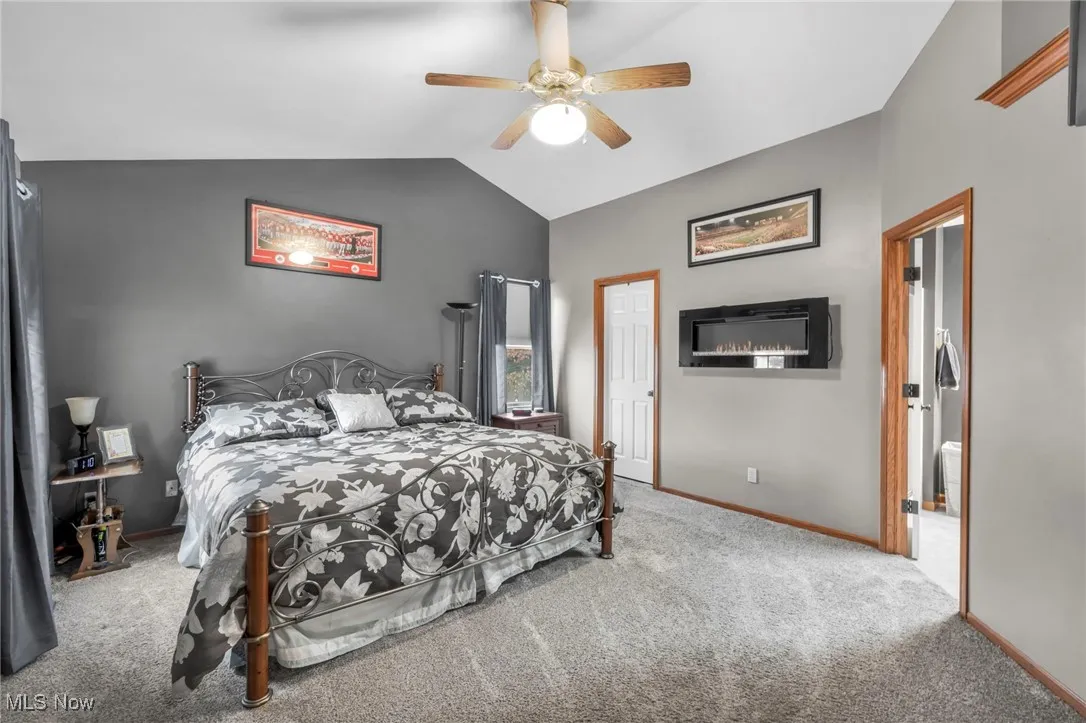 Bedroom featuring carpet flooring, lofted ceiling, a ceiling fan, and an electric fireplace