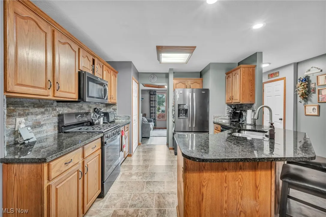 Kitchen with stainless steel appliances, a peninsula, decorative backsplash, dark stone counters, and a breakfast bar