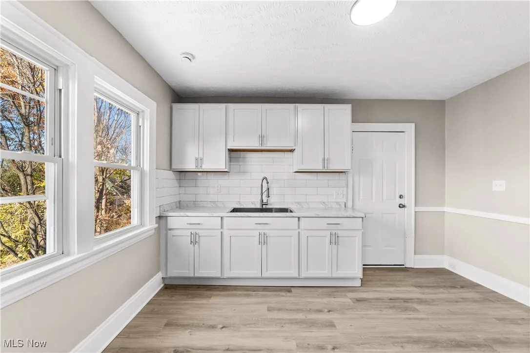 Kitchen with light countertops, light wood-style flooring, tasteful backsplash, white cabinetry, and a textured ceiling
