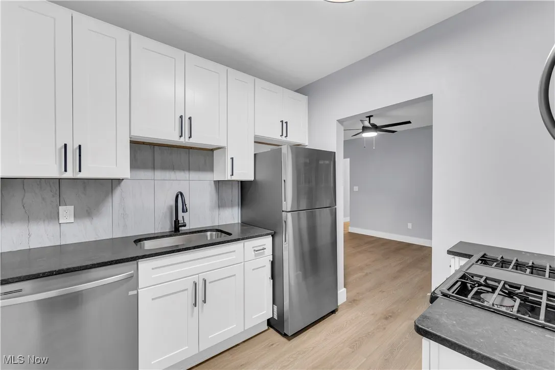 Kitchen with stainless steel appliances, decorative backsplash, white cabinetry, and dark stone counters