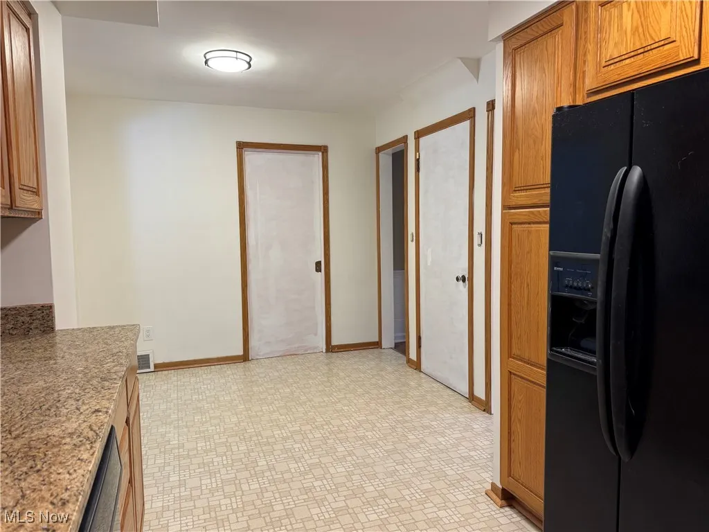 Kitchen with black fridge, brown cabinets, light stone countertops, and light floors