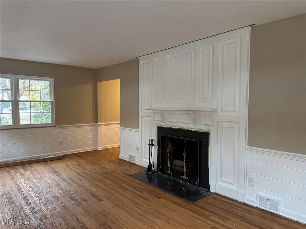 Unfurnished living room with wainscoting, a fireplace, dark wood-style floors, and a decorative wall
