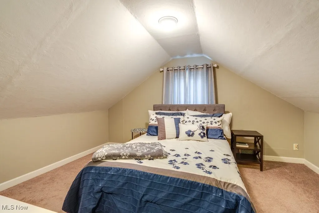 Bedroom featuring light carpet, vaulted ceiling, and a textured ceiling