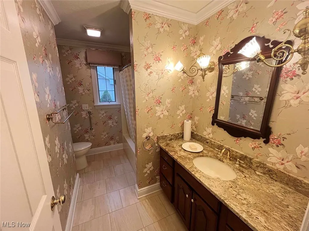 Bathroom featuring wallpapered walls, crown molding, vanity, light tile patterned floors, and shower / bath combo with shower curtain