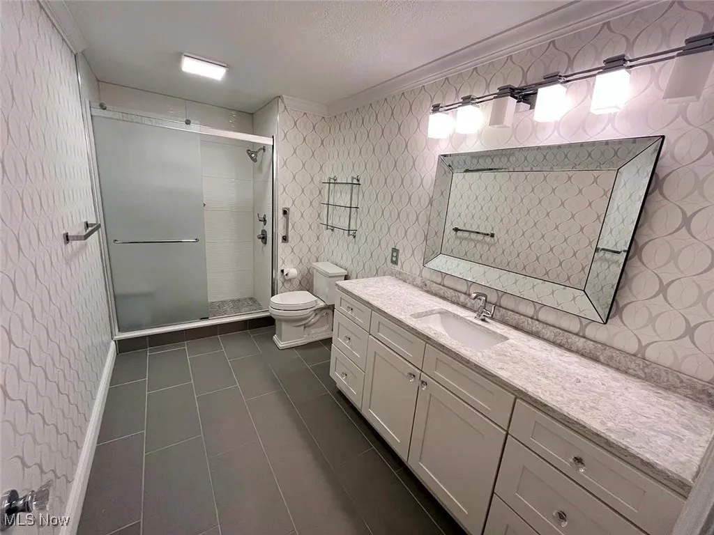Bathroom with wallpapered walls, a shower stall, vanity, dark tile patterned flooring, and a textured ceiling
