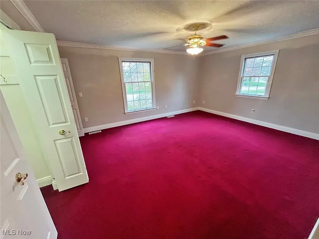 Bedroom with crown molding, dark carpet, a textured ceiling, healthy amount of natural light, and a ceiling fan