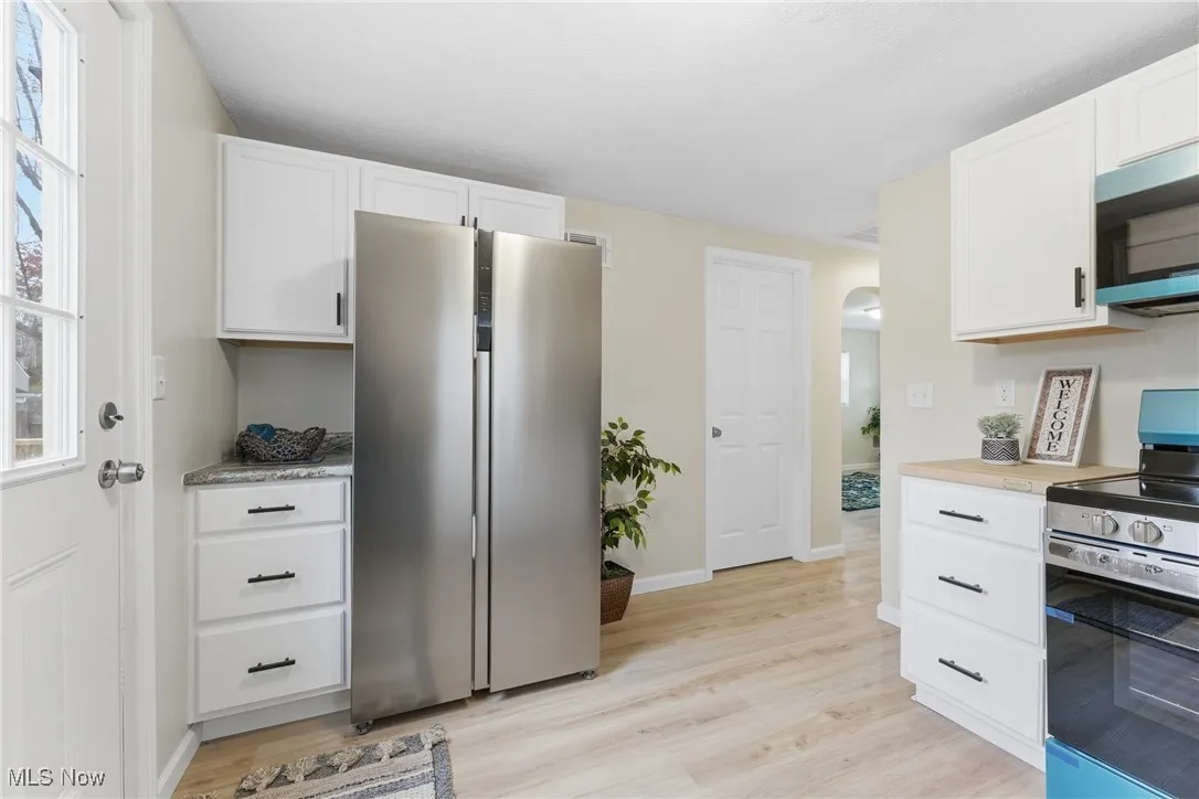 Kitchen with appliances with stainless steel finishes, arched walkways, white cabinets, light countertops, and light wood finished floors