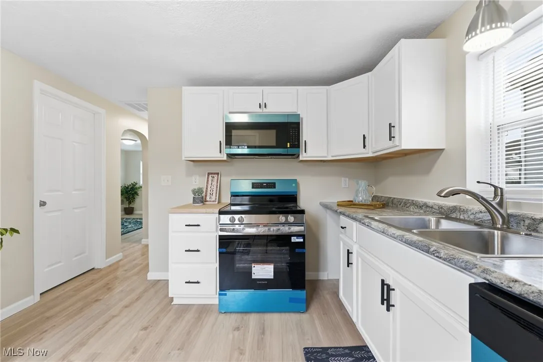Kitchen featuring stainless steel appliances, arched walkways, light wood-type flooring, white cabinets, and light countertops