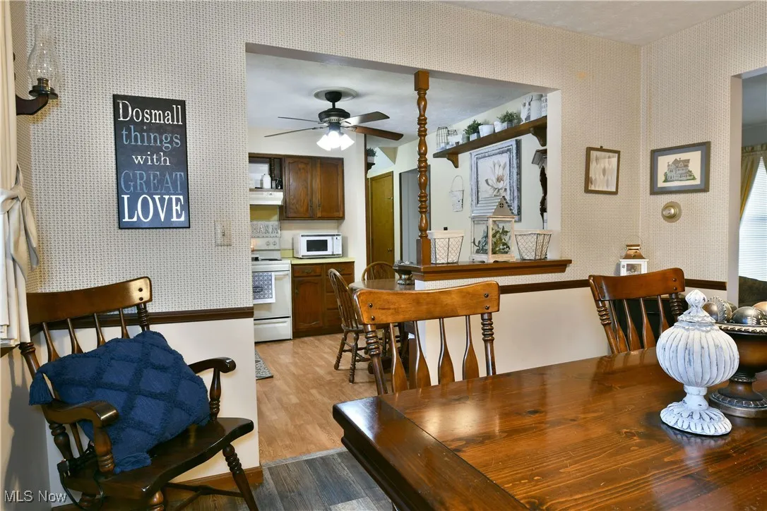Dining space with wallpapered walls, light wood-style flooring, and ceiling fan